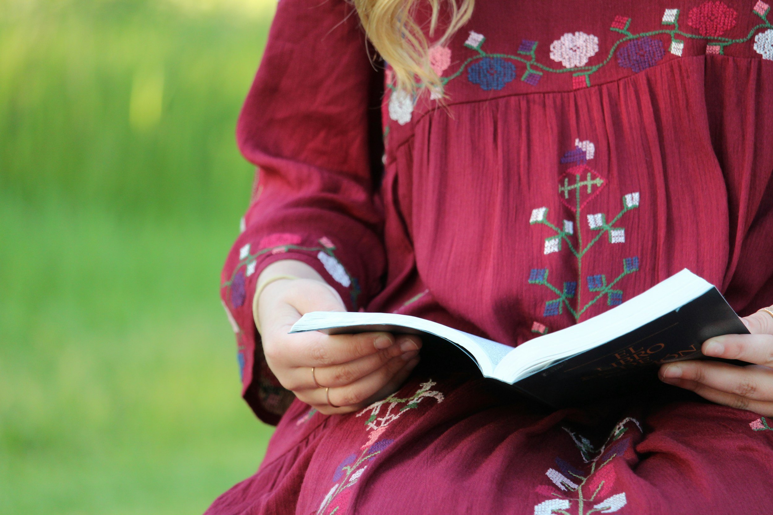 Person in a red embroidered dress sitting outdoors and reading a book.