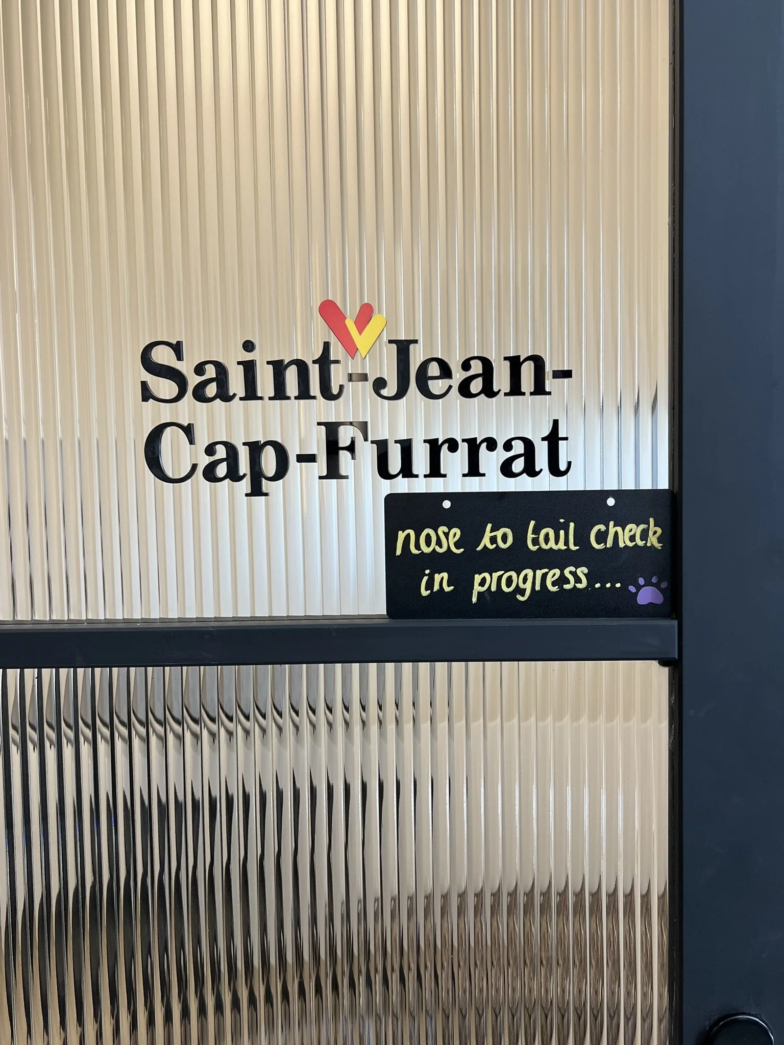 Sign for Saint-Jean-Cap-Furrat with a small blackboard that says 'nose to tail check in progress...' and a purple paw print.