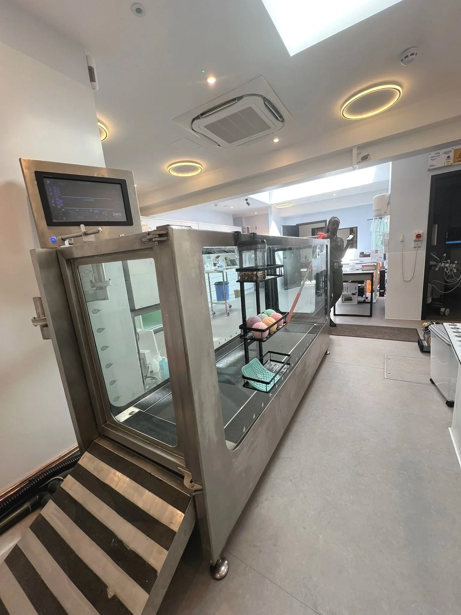 A stainless steel ice cream display case with a glass front, containing colorful scoops of ice cream and a small basket, located in a modern, well-lit room.