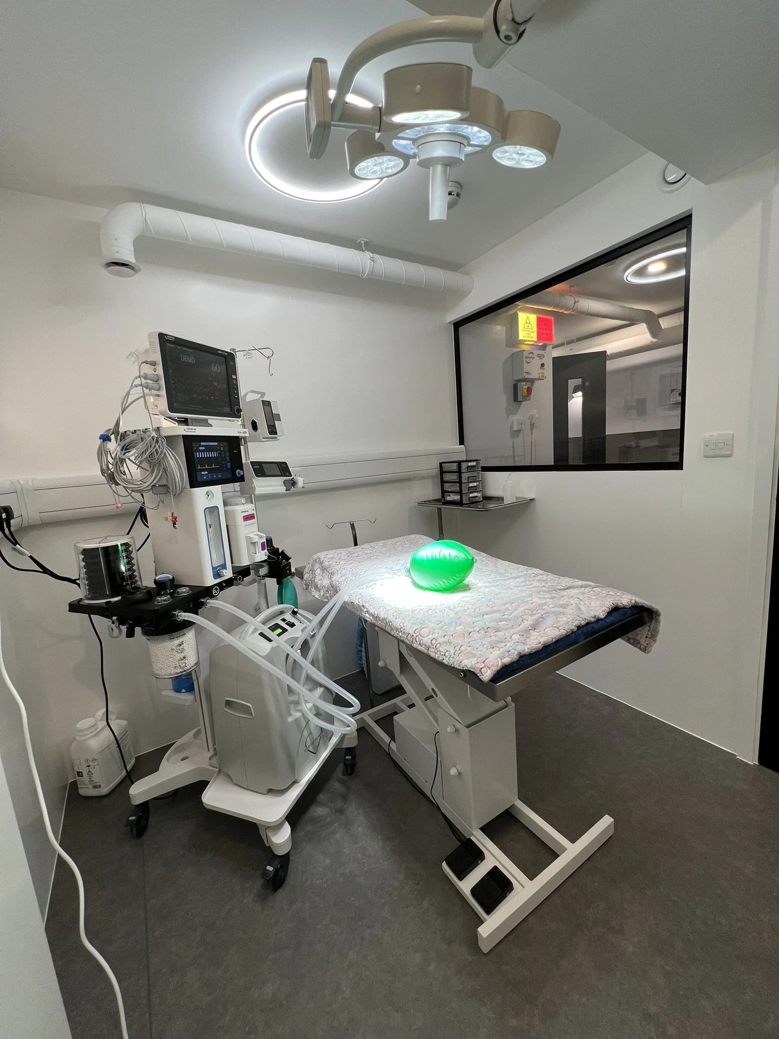 A hospital operating room with medical equipment and a patient bed covered with a quilt, with a green glowing object on top.