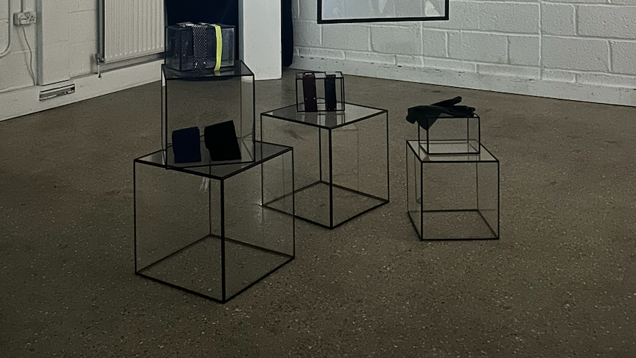 Minimalist display with transparent cube tables holding small objects in a modern interior space.