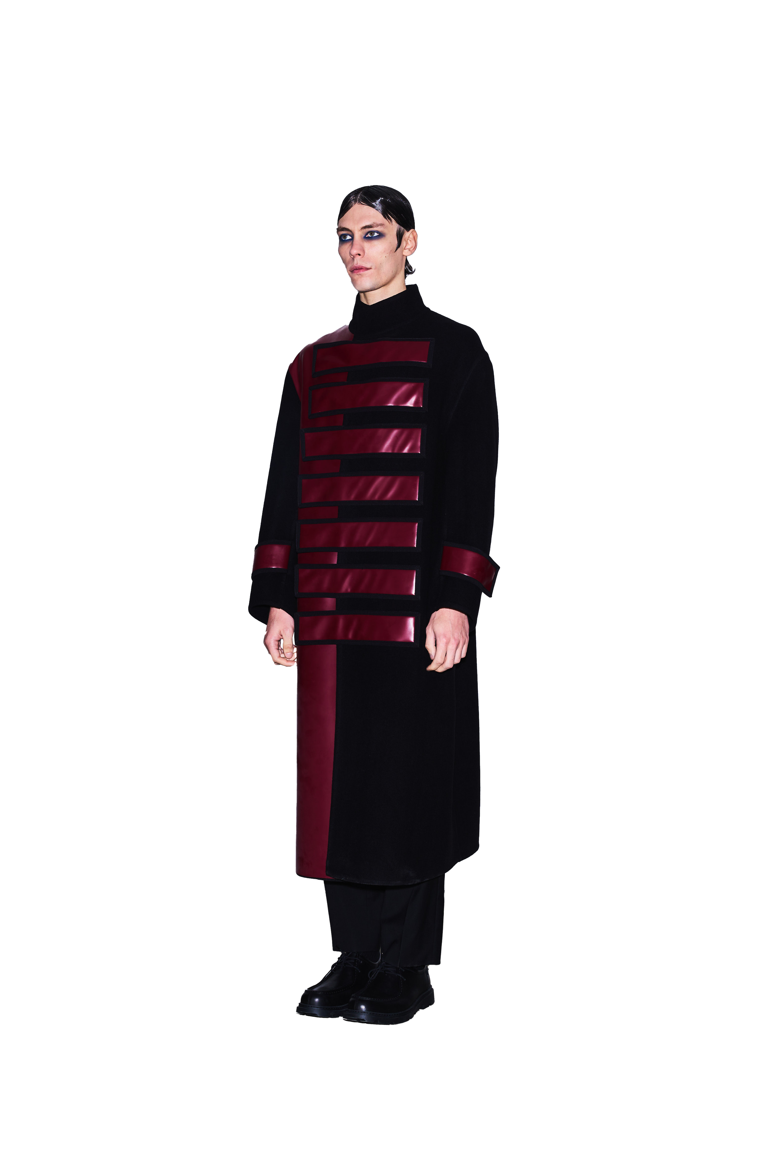 Person wearing a long black coat with red accents and patterns, standing against a white background.