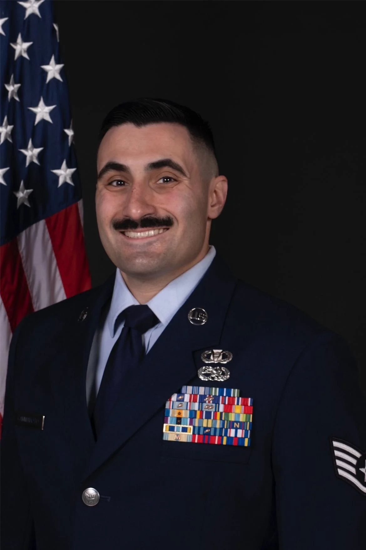 A smiling man in a U.S. Air Force uniform standing in front of an American flag.