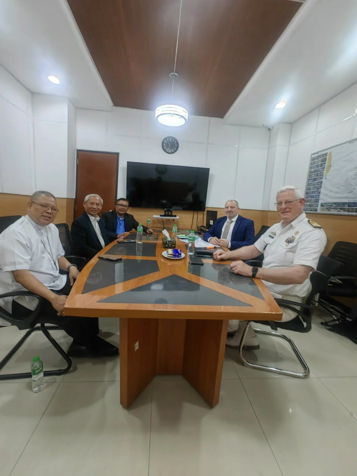 Five men sitting around a conference table with water bottles and laptops in a meeting room.