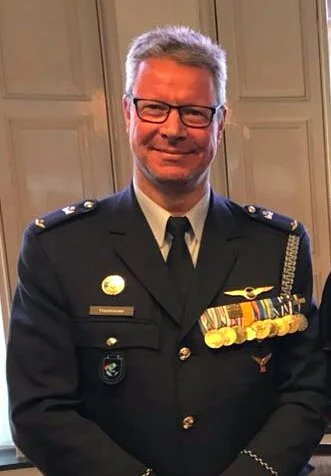 A man in a military uniform with medals, posing indoors with a smile.