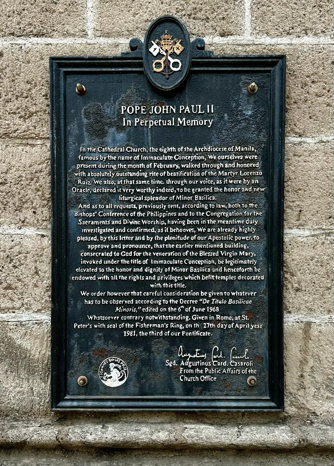 A commemorative plaque dedicated to Pope John Paul II, located on a stone wall. The plaque features the Pope's title and a message about his recognition for the sacred celebration of the Virgin Mary, with an official seal and signature at the bottom.