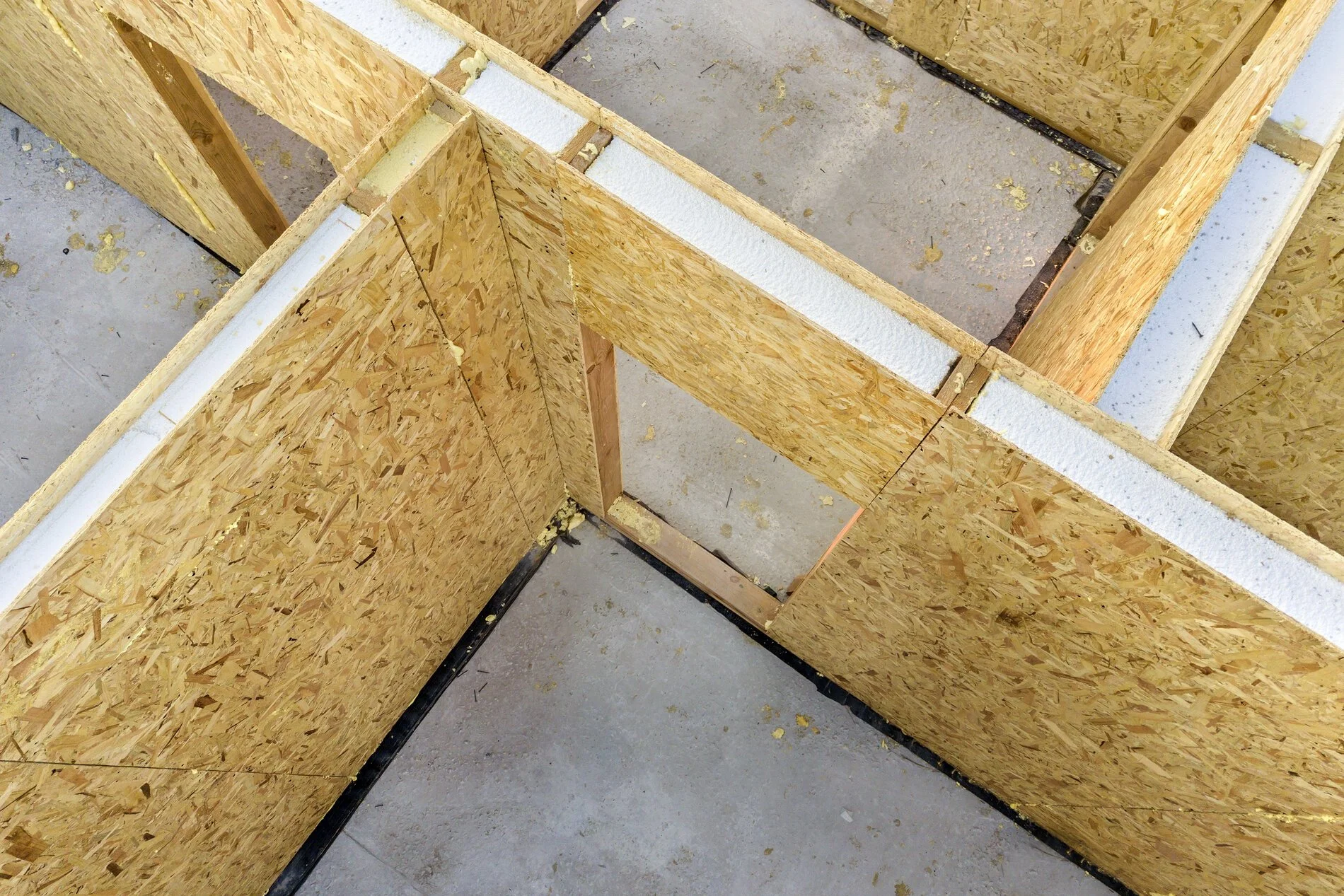 Interior framing of a building under construction with wooden OSB panels on a concrete floor, some panels cut out to form door openings.