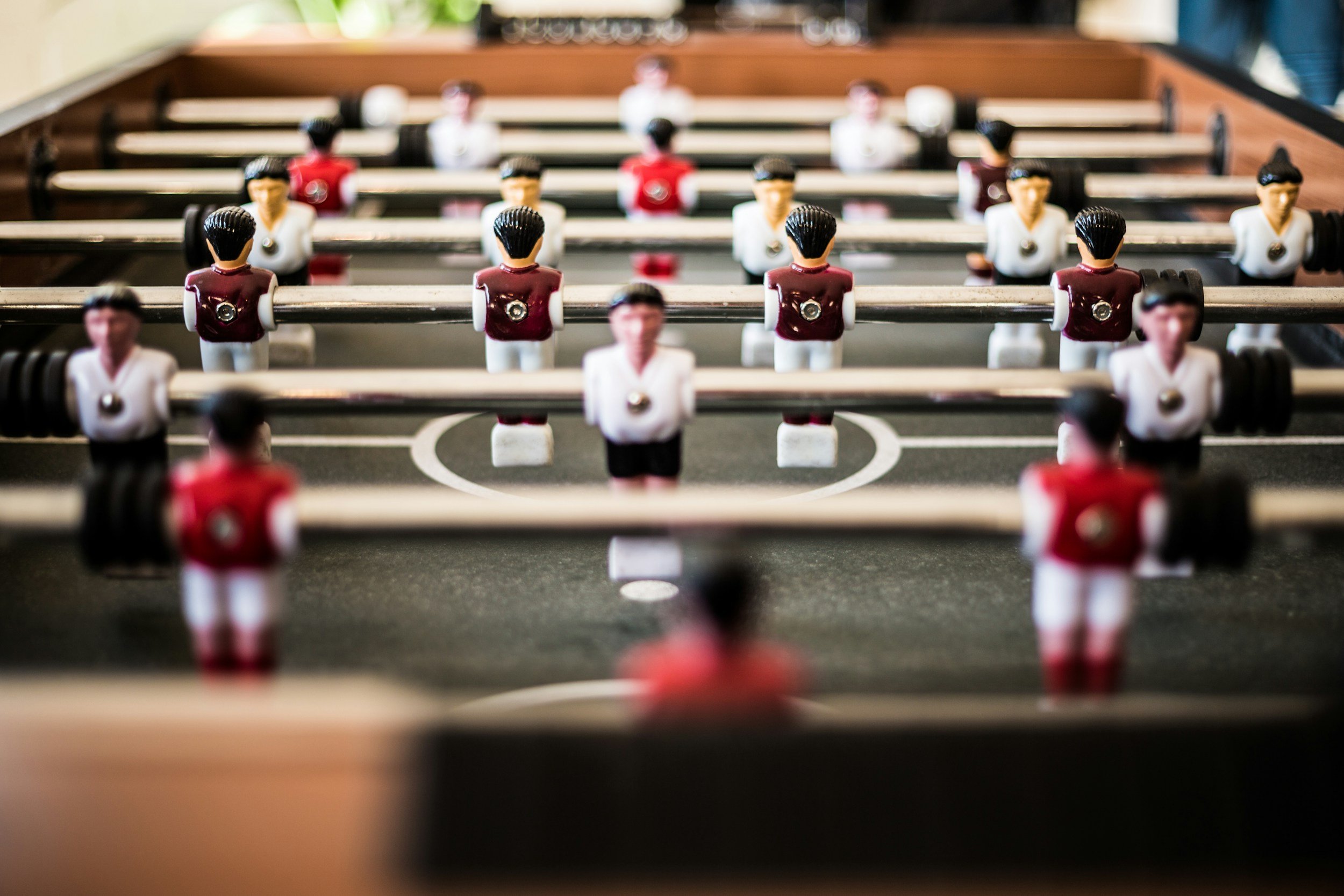 Close-up of a foosball table with plastic players in white and red uniforms, focusing on the front row.