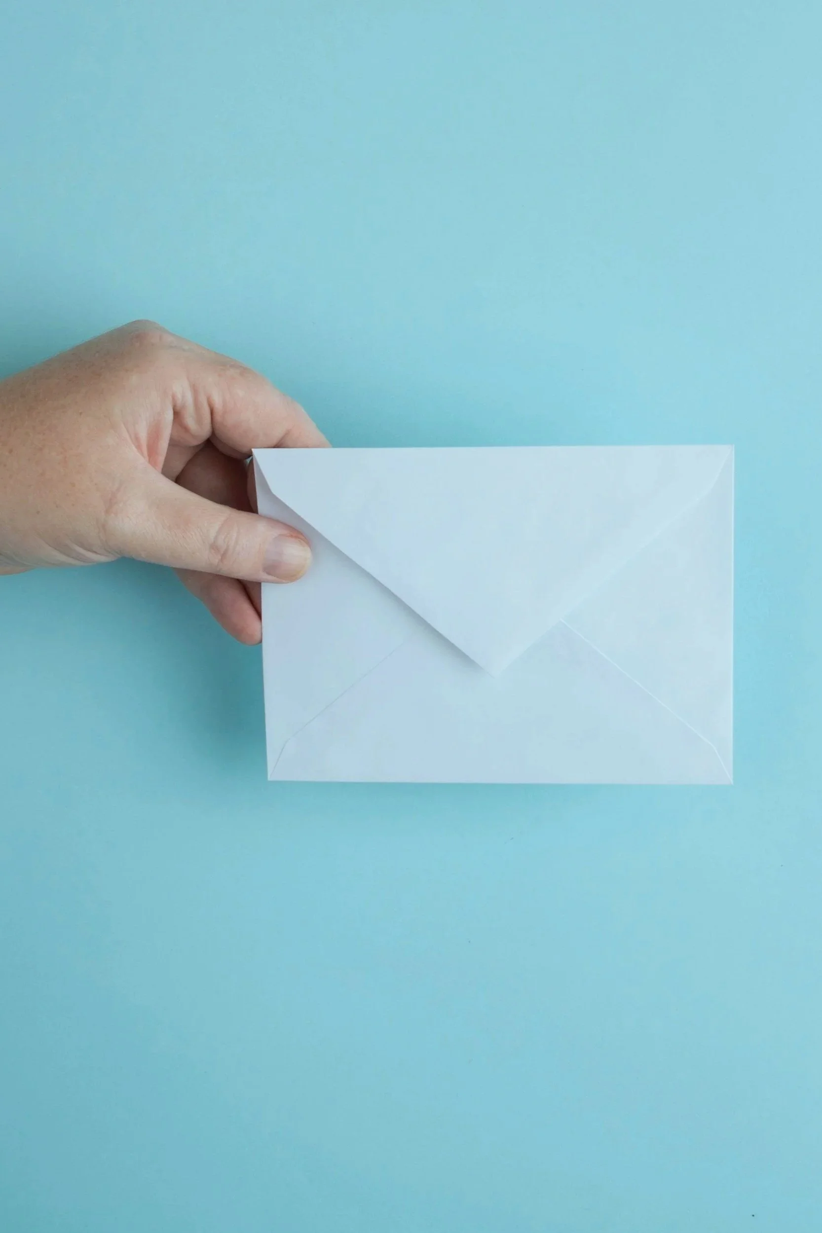 A hand holding a white paper envelope against a light blue background.