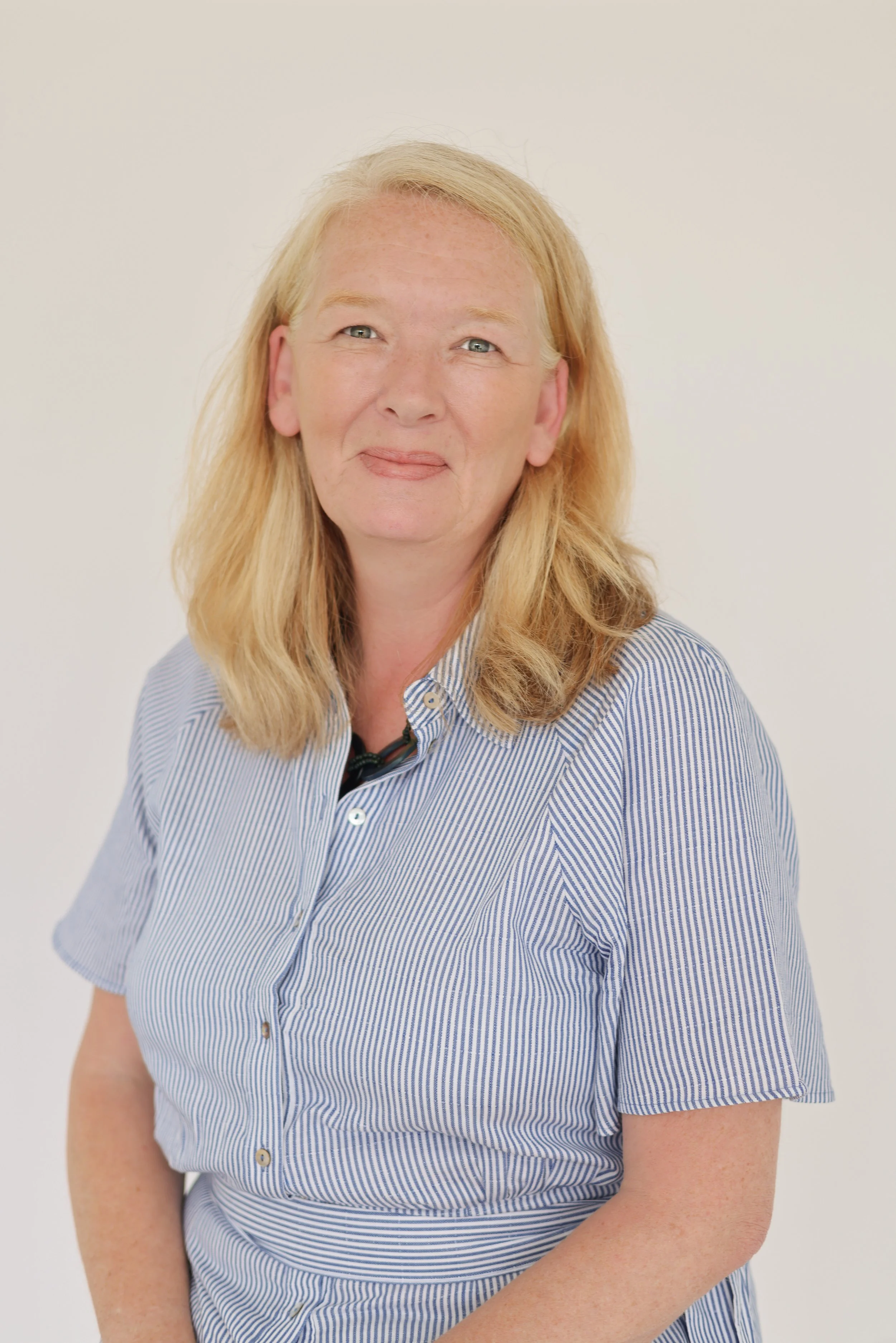 A headshot of Johanna. Johanna has red hair, blue eyes, and light skin, wearing a blue and white striped button-up shirt, standing against a plain white background.