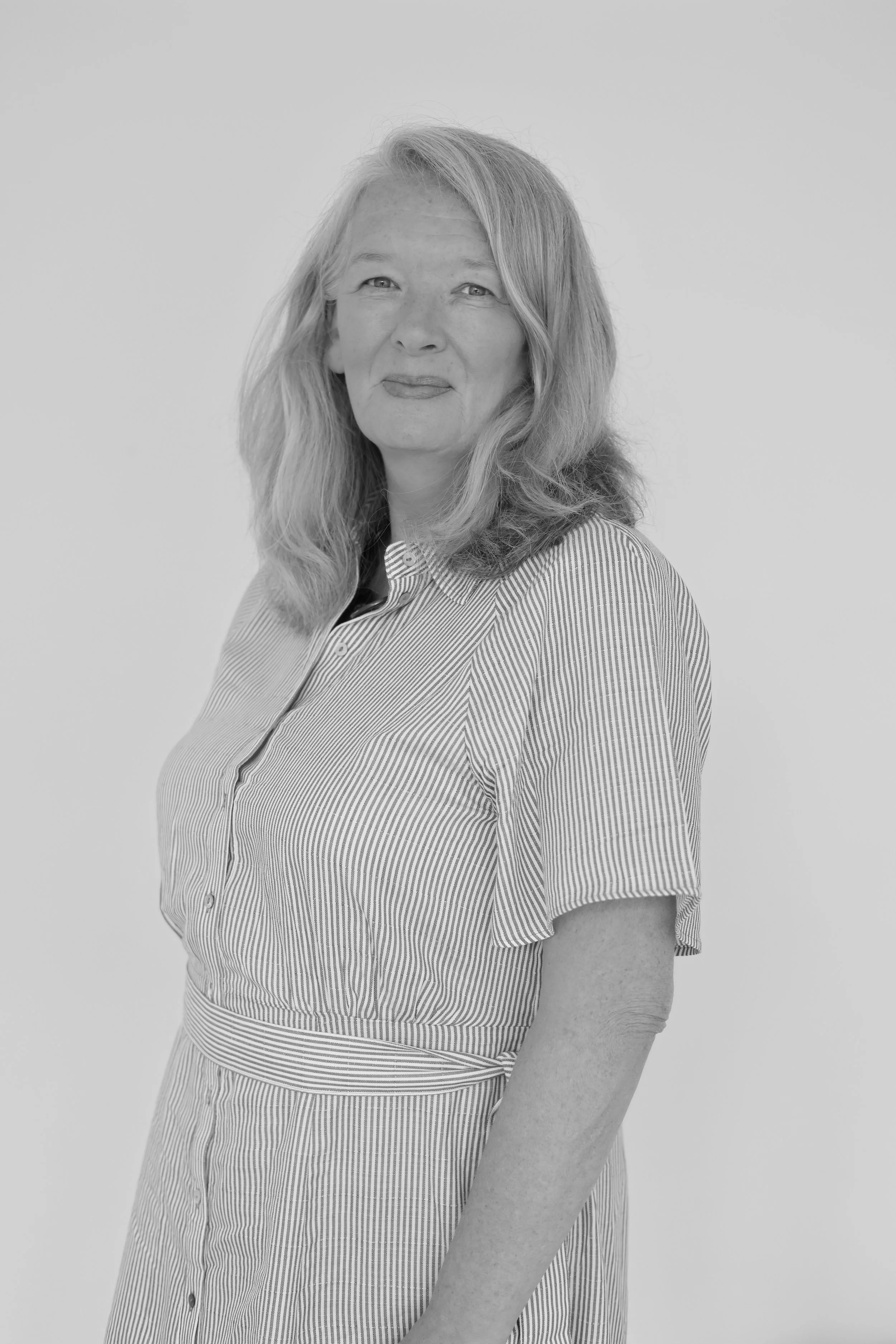 A black and white portrait of Johanna with wavy hair, wearing a vertically striped dress with short sleeves, standing against a plain background.