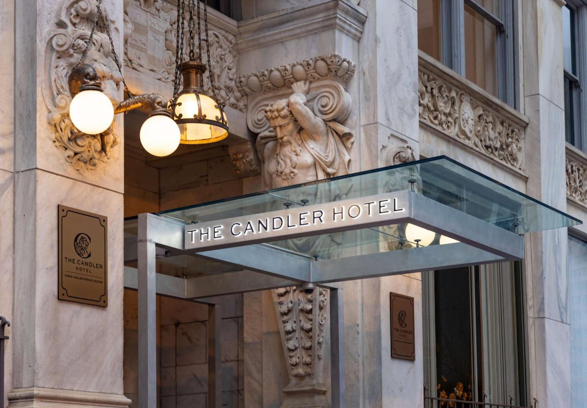 Exterior of the Candleer Hotel with ornate stone carvings, a decorative bust of a bearded man, and a sign displaying the hotel name.