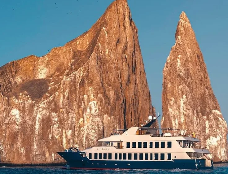 Luxury yacht sailing near large rocky cliffs with blue sky background.
