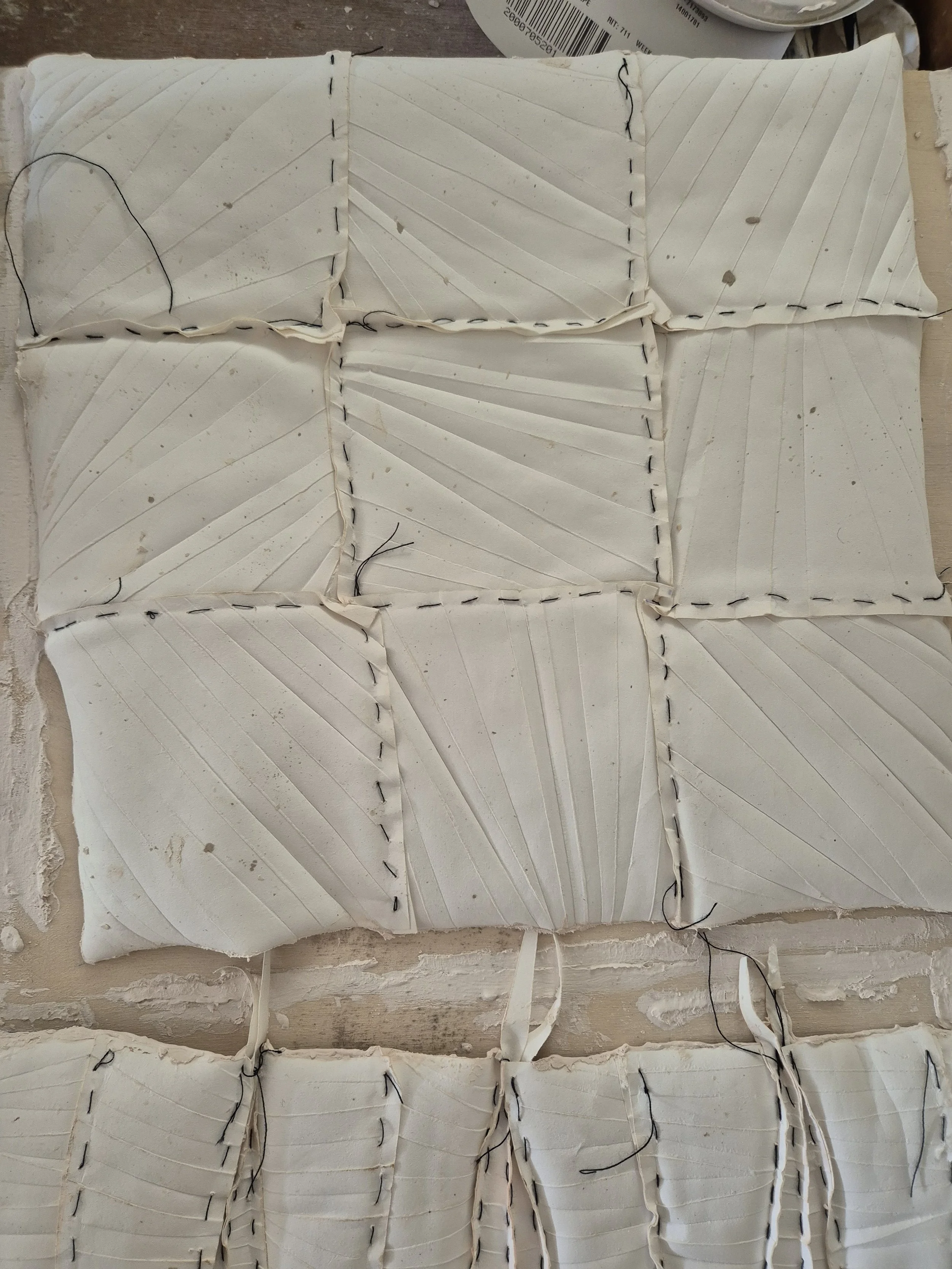 Wit kunstwerk met vierkanten en zwarte naden, textieltextuur.