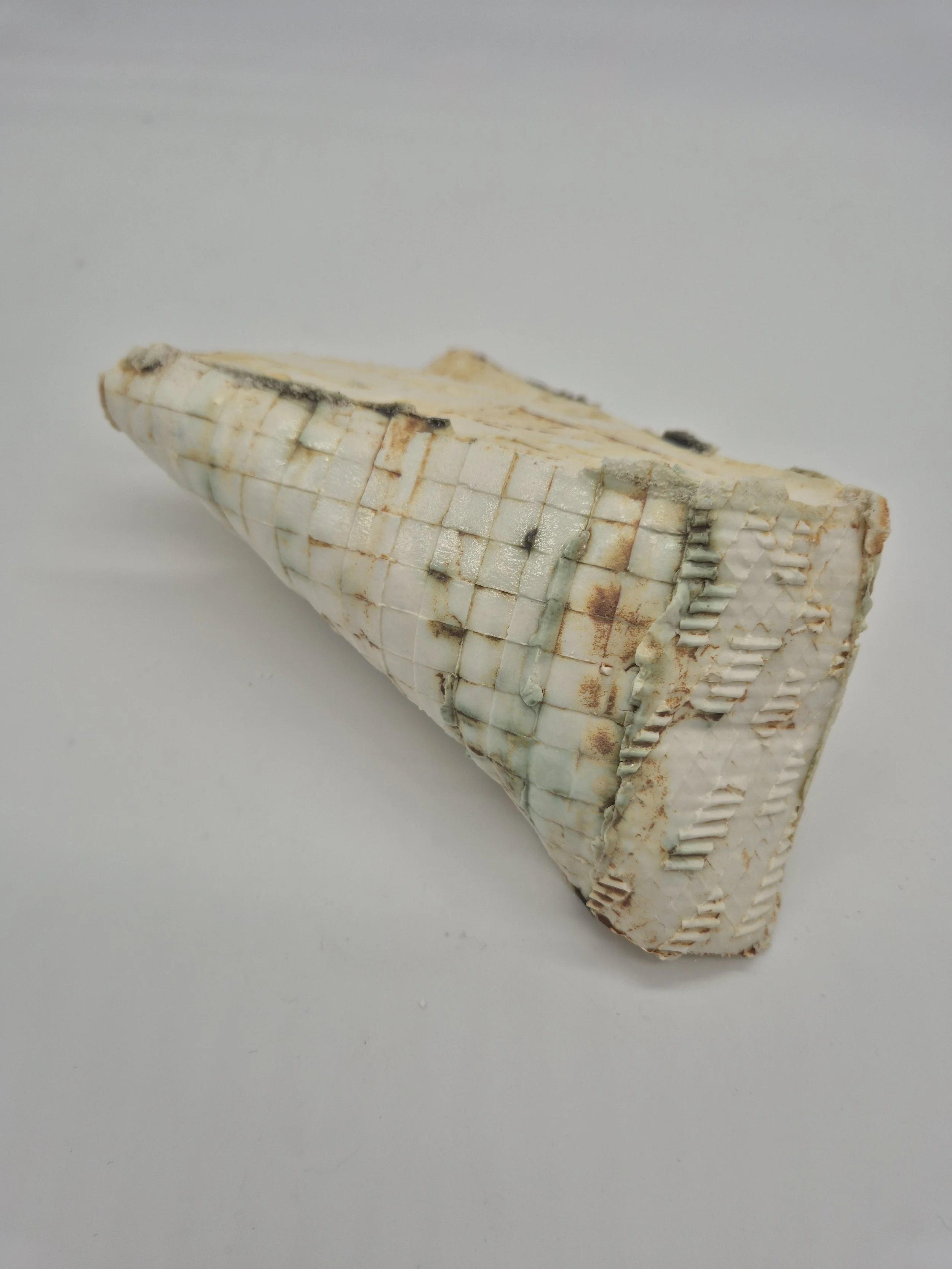 Een wit stenen keramisch object op een witte achtergrond, met een gerasterd patroon en enkele verkleuringen.