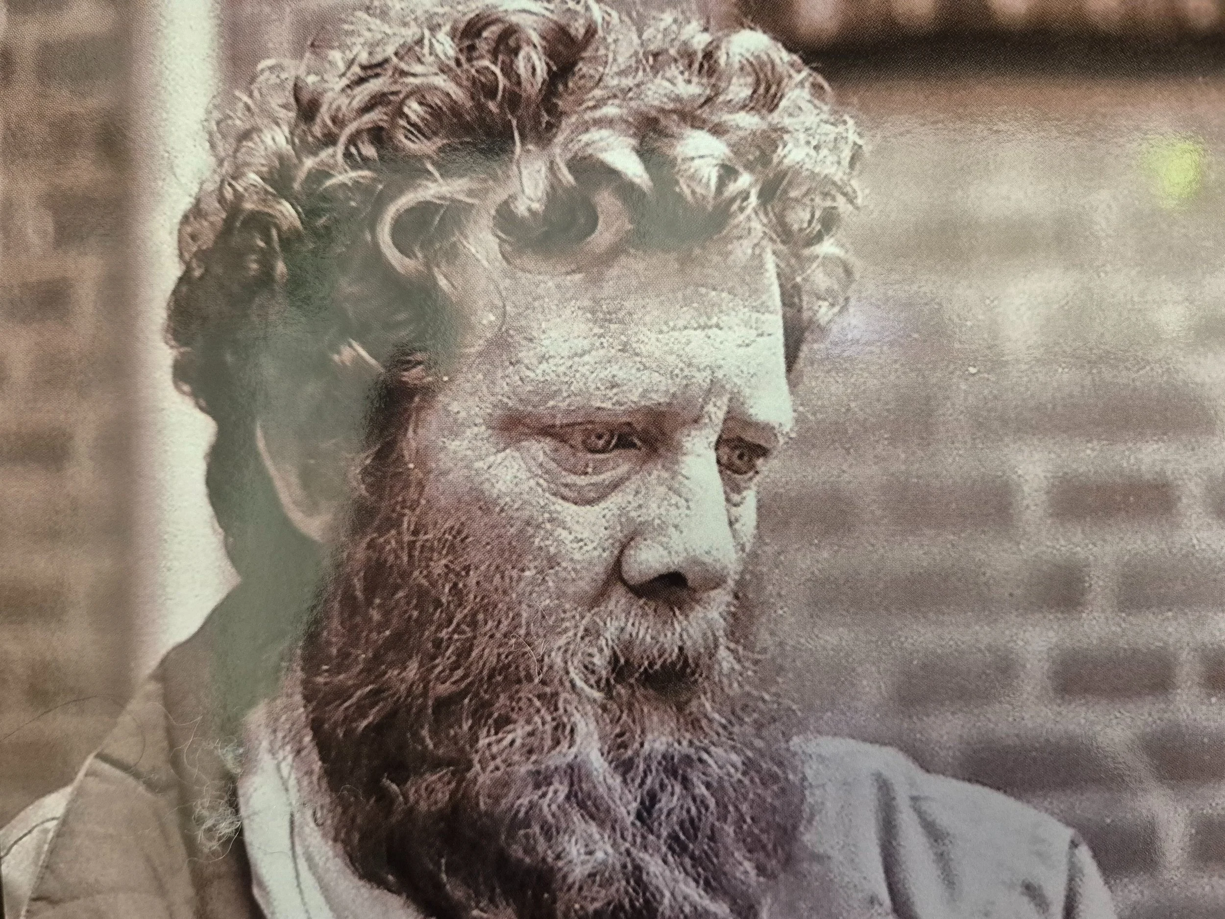 Vintage portret van een man met krullend haar en een baard, naar beneden kijkend. Rotterdamse dak- en thuisloze.