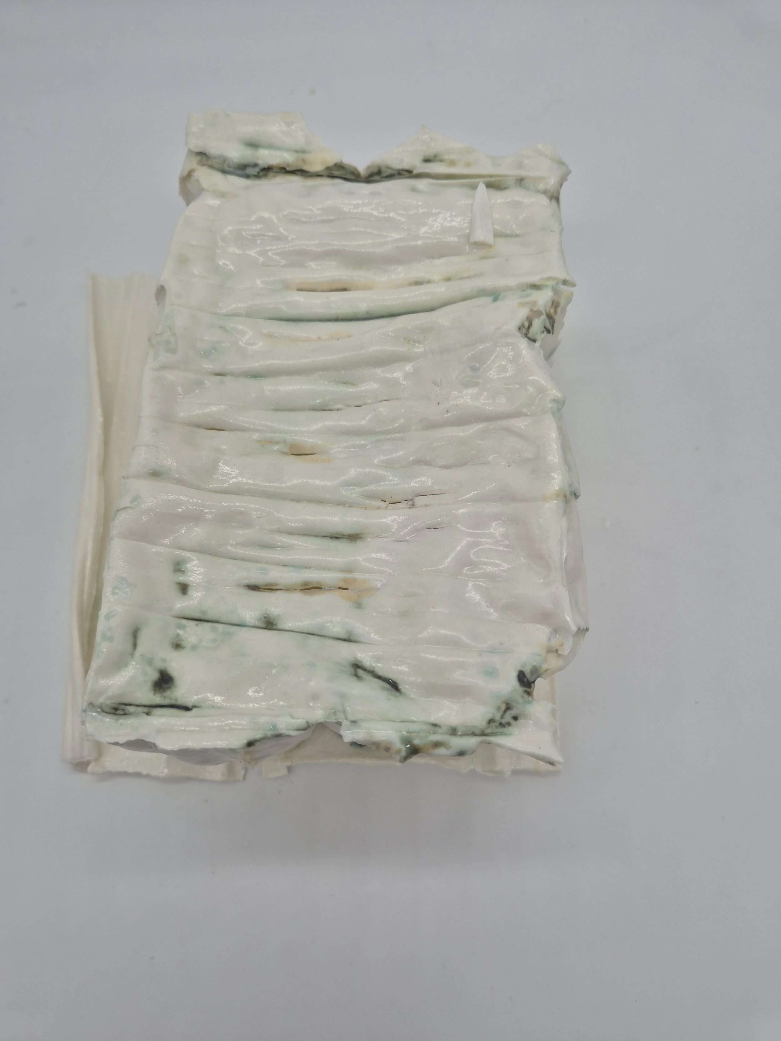 Gelaagd wit keramische sculptuur met een gegolfde textuur en gaten.