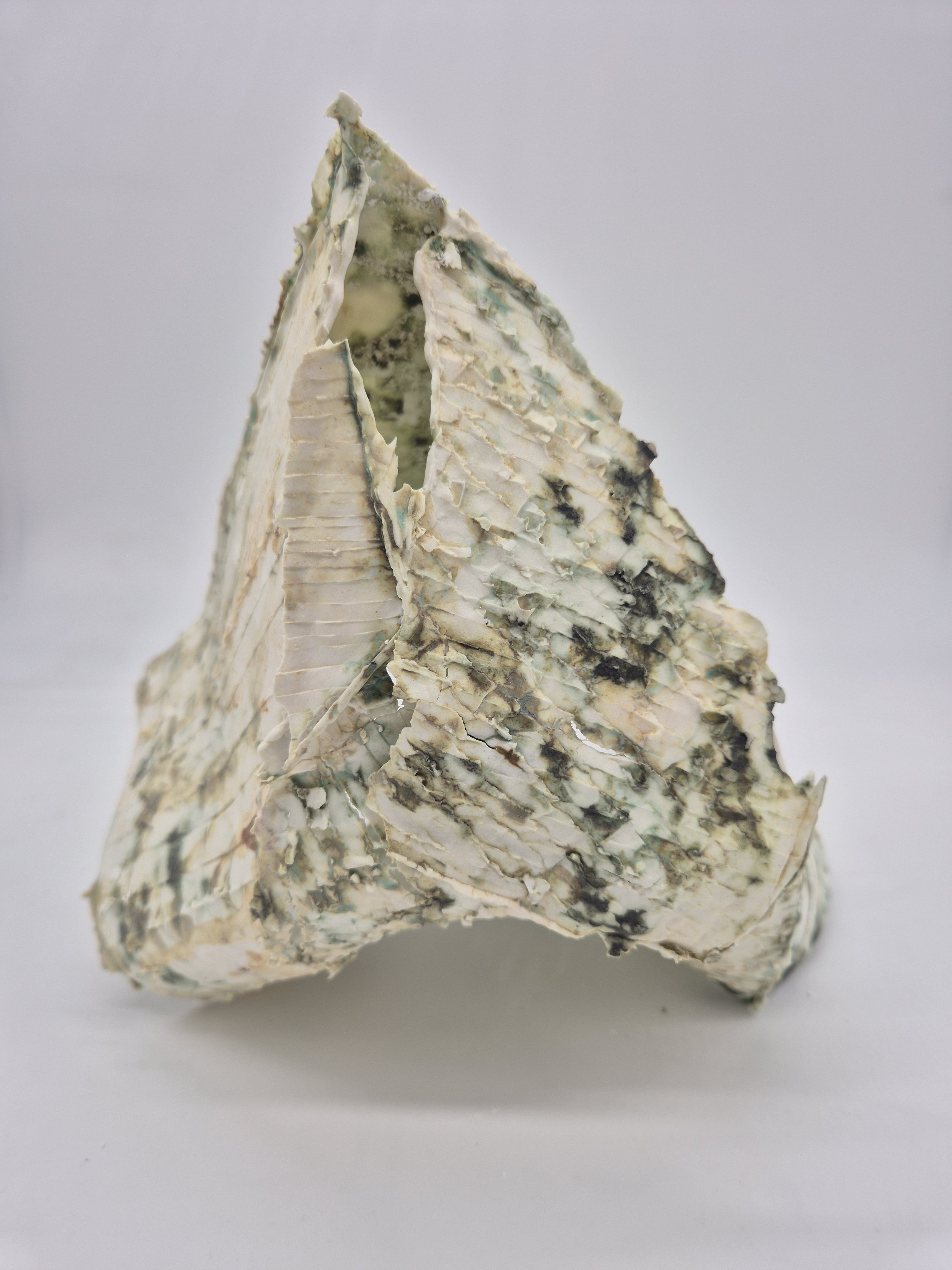 Close-up van een driekhoekige, lichtblauw-gekleurde, fragile, keramiek object, tegen een neutrale achtergrond.