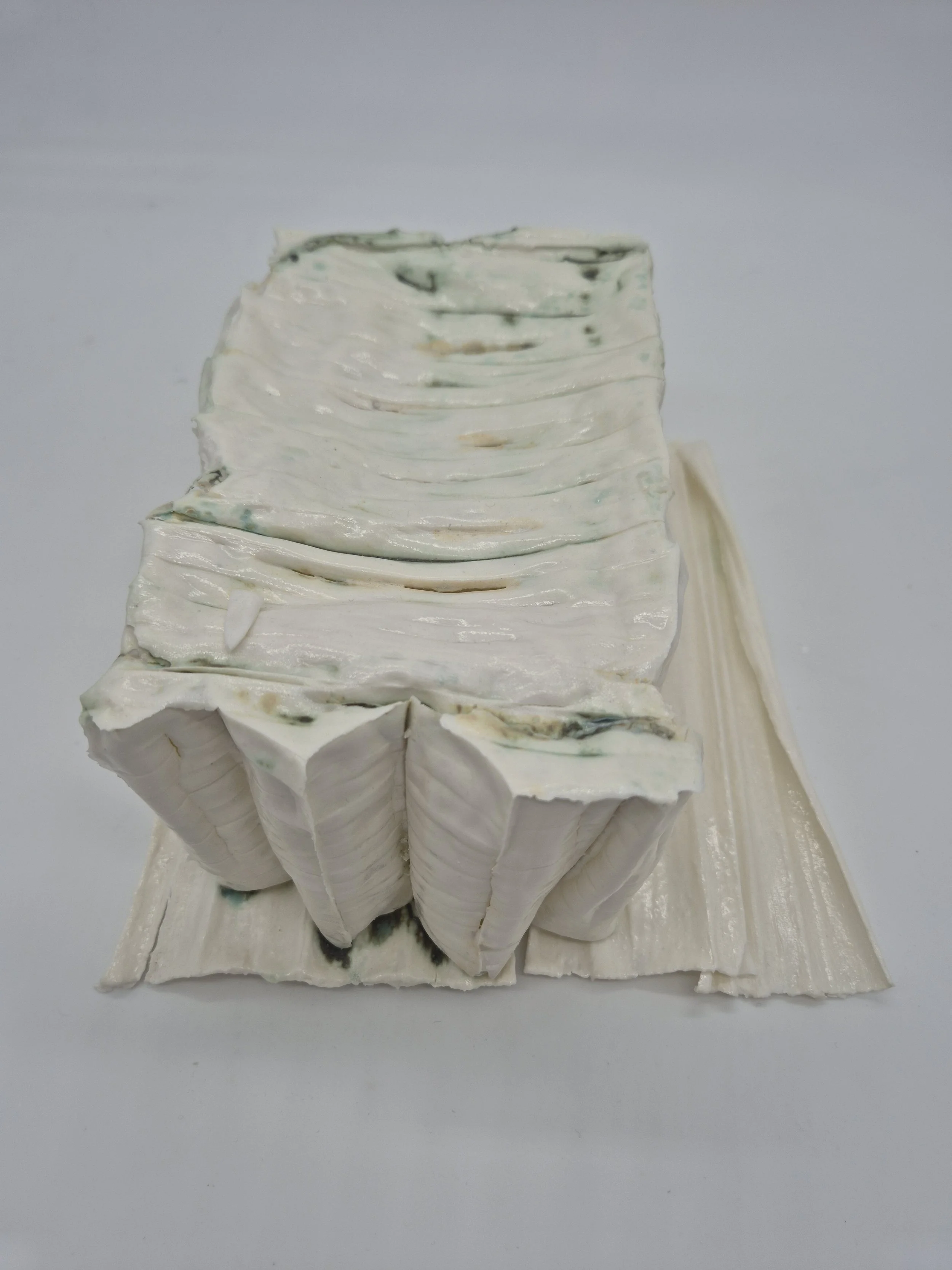 Gelaagde witte keramische structuur met groene vlekken en opvallende textuur, op een witte achtergrond.