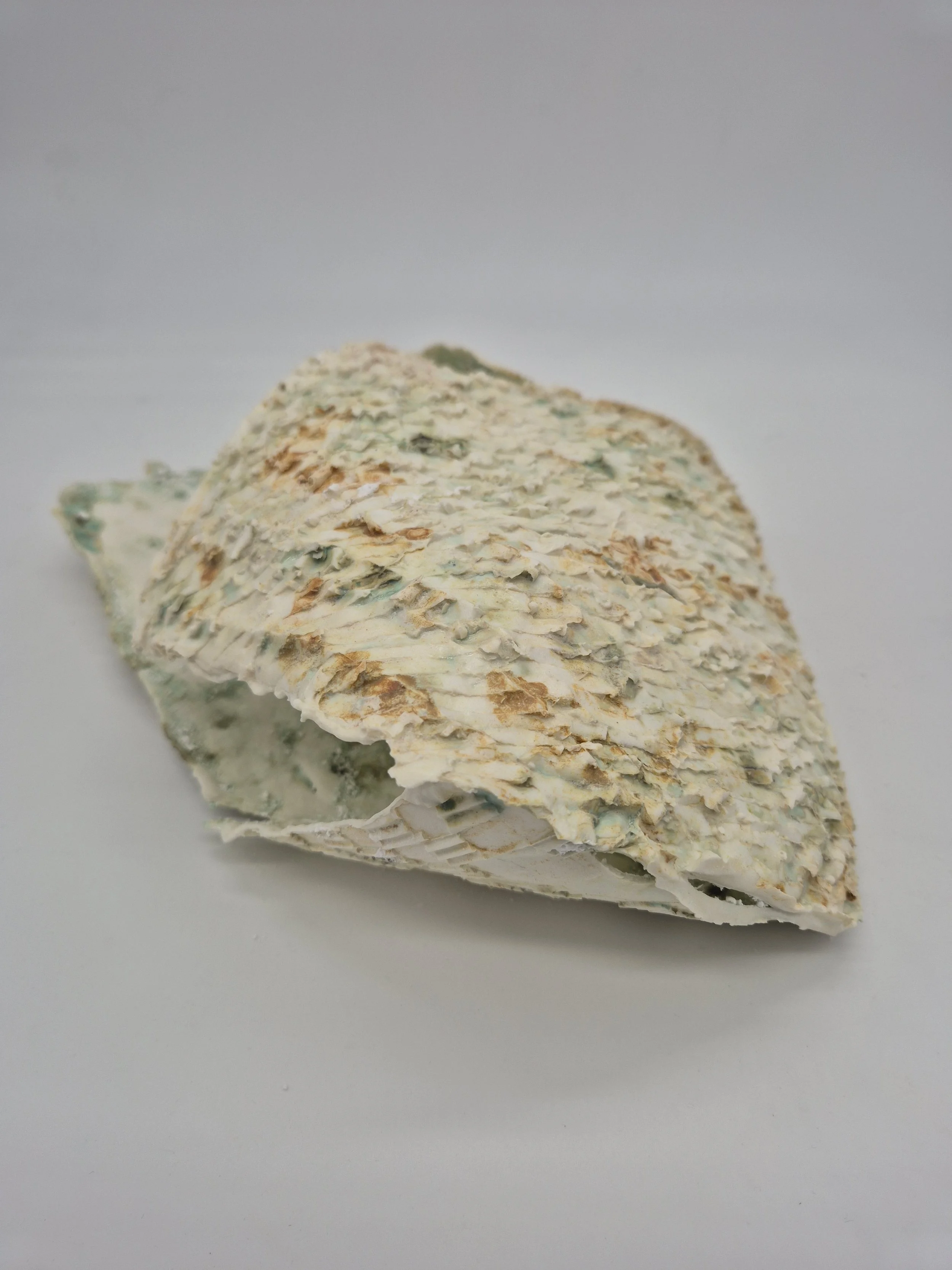 Ruwe keramische sculptuur met textuur in neutrale kleuren, op witte achtergrond.