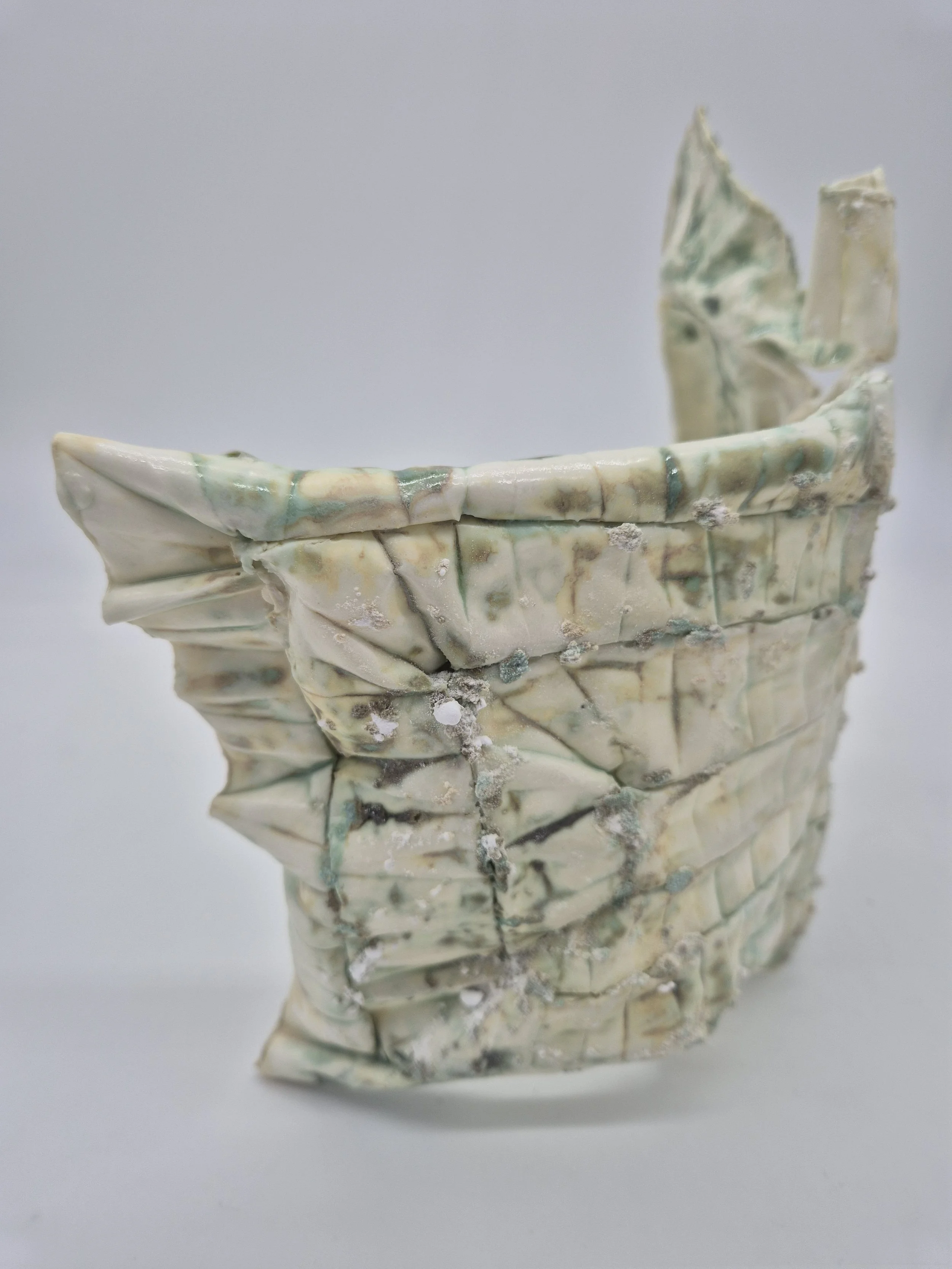 Gevouwen stuk keramiek met beige en groene tinten tegen een witte achtergrond.