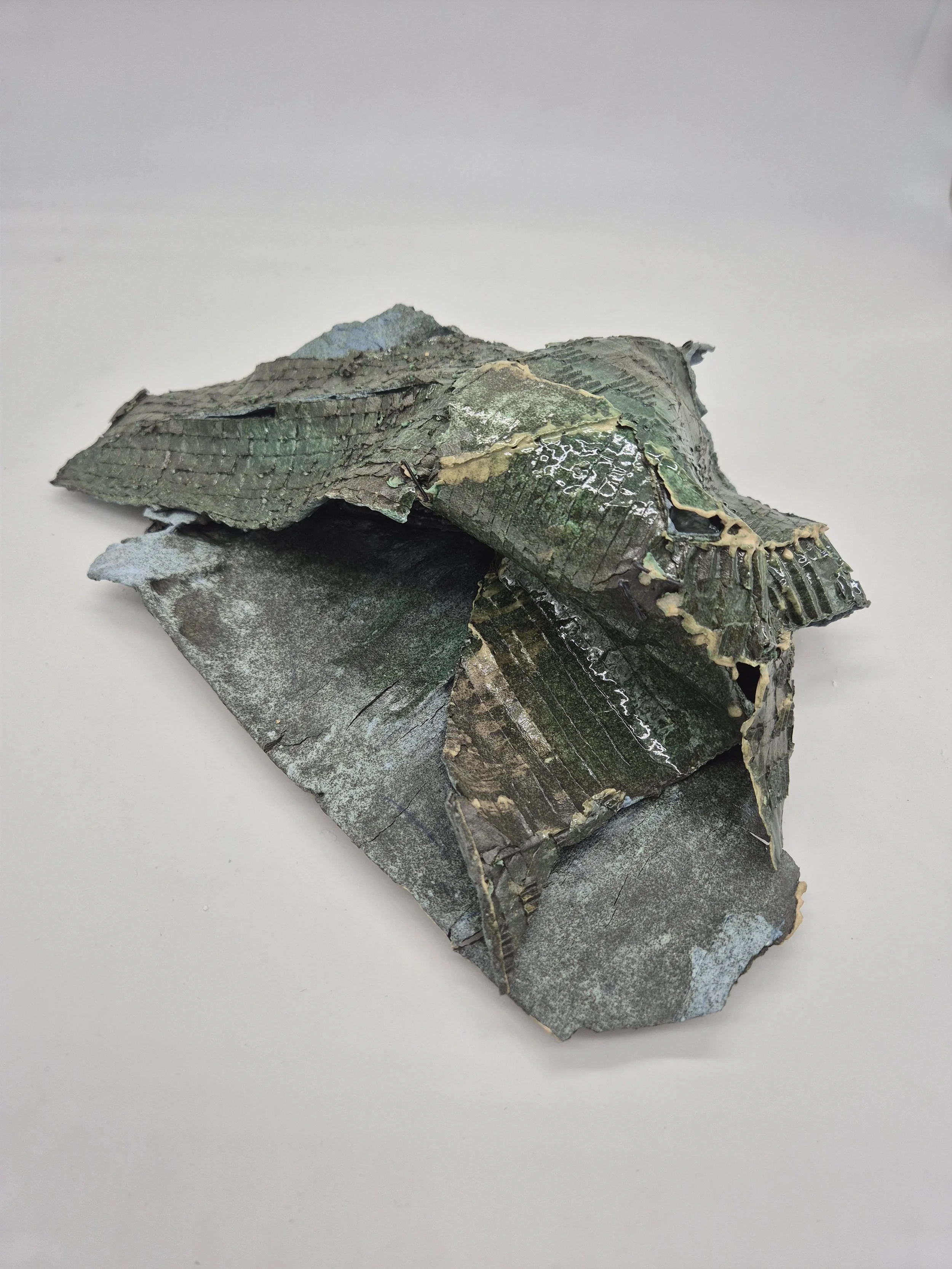 Abstract keramisch beeld dat lijkt op een gekreukeld stuk karton met afbladderende verf en textuur.