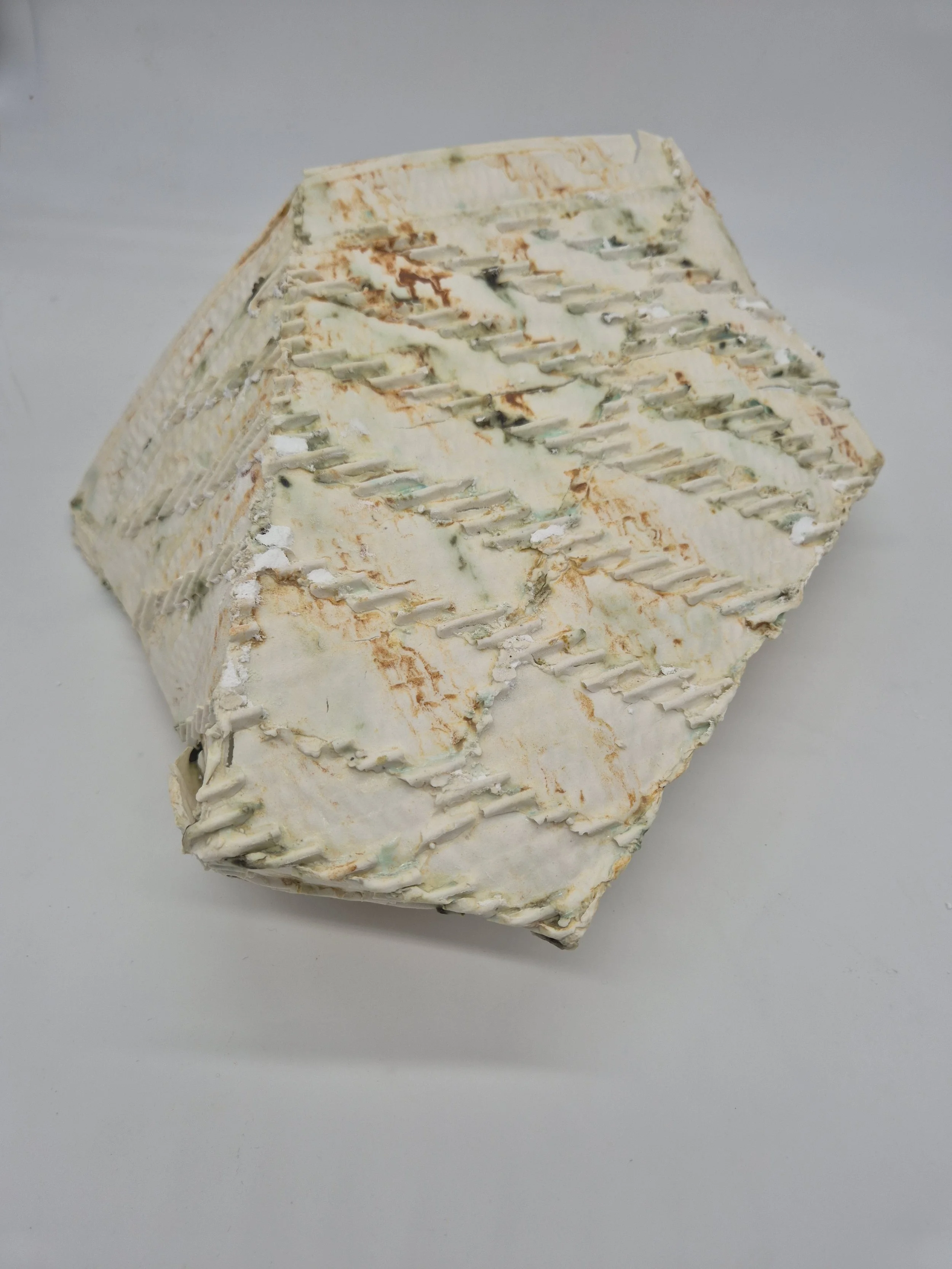 Keramisch object met een unieke textuur en kleuren, waaronder beige en groene tinten, geplaatst tegen een witte achtergrond.