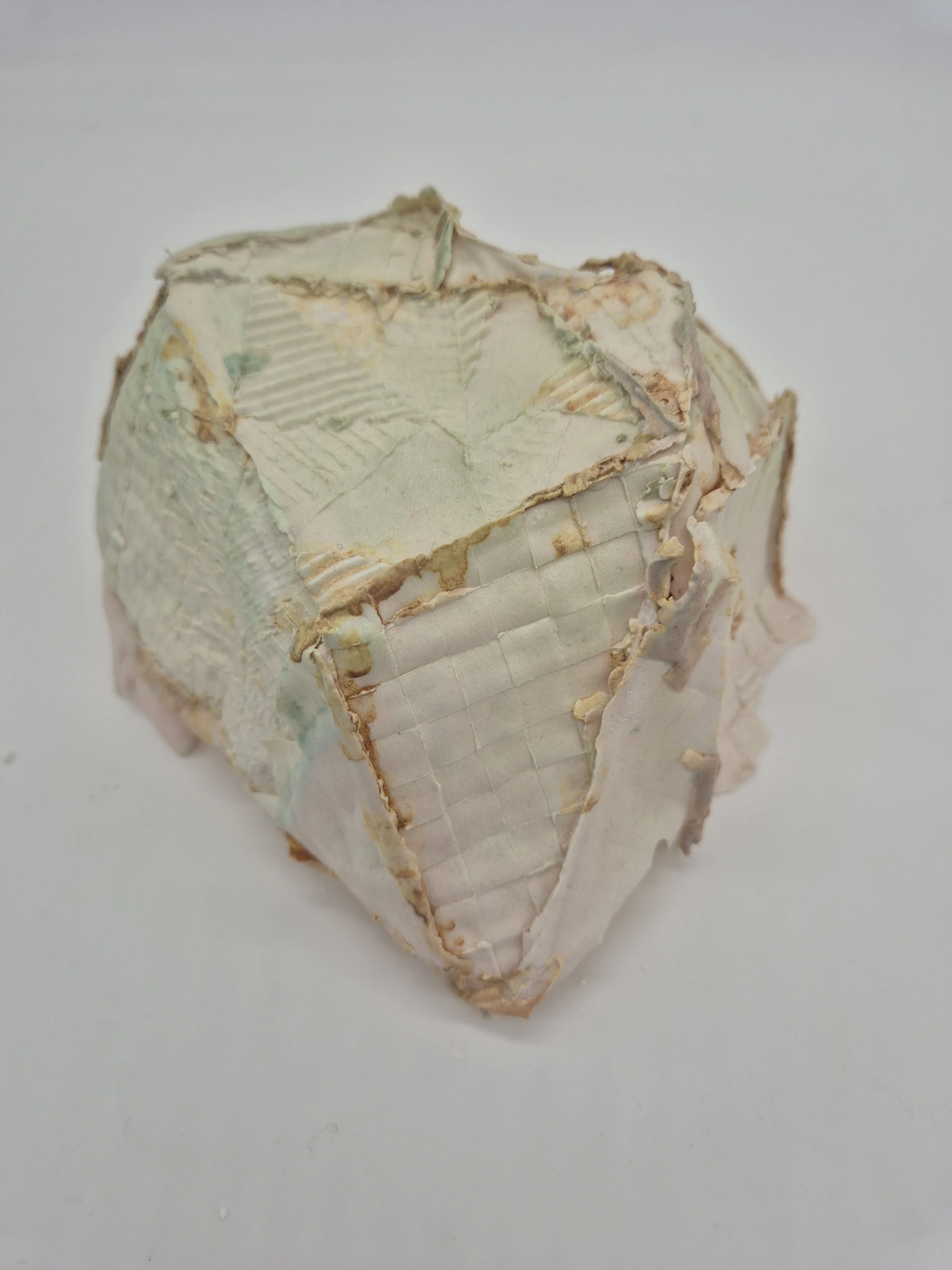 Ongelijk gevormd keramiekobject met zichtbare naden en verweerde delen tegen een witte achtergrond.