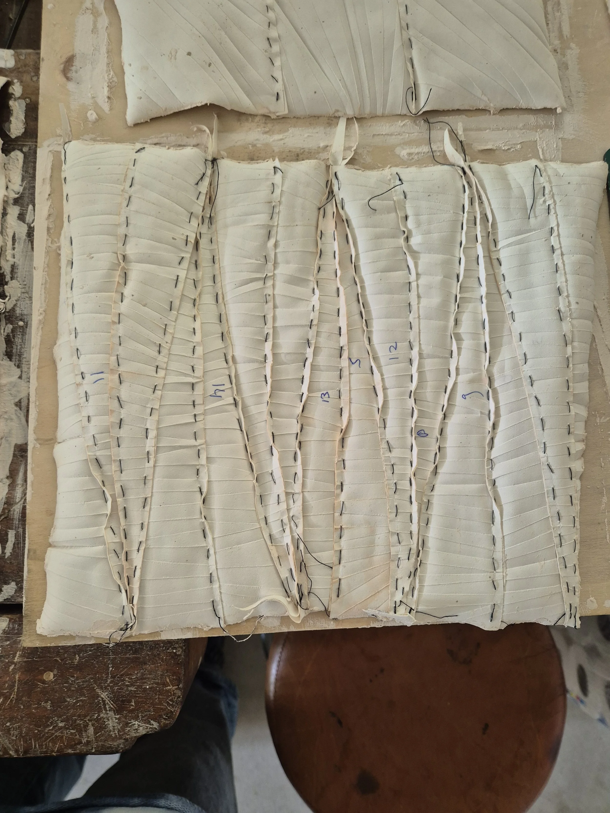 Houten tafel met keramisch kunstwerk met gevouwen witte klei en zwarte stiksels.