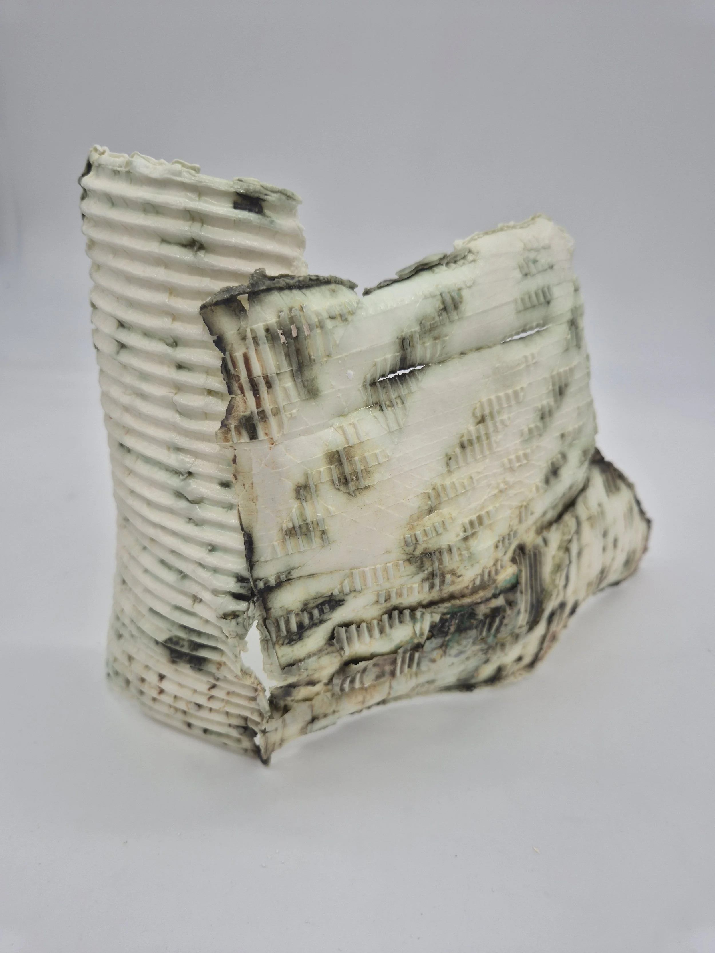 Abstract keramisch beeld met geribbelde textuur en groenachtige tinten, tegen een grijze achtergrond.