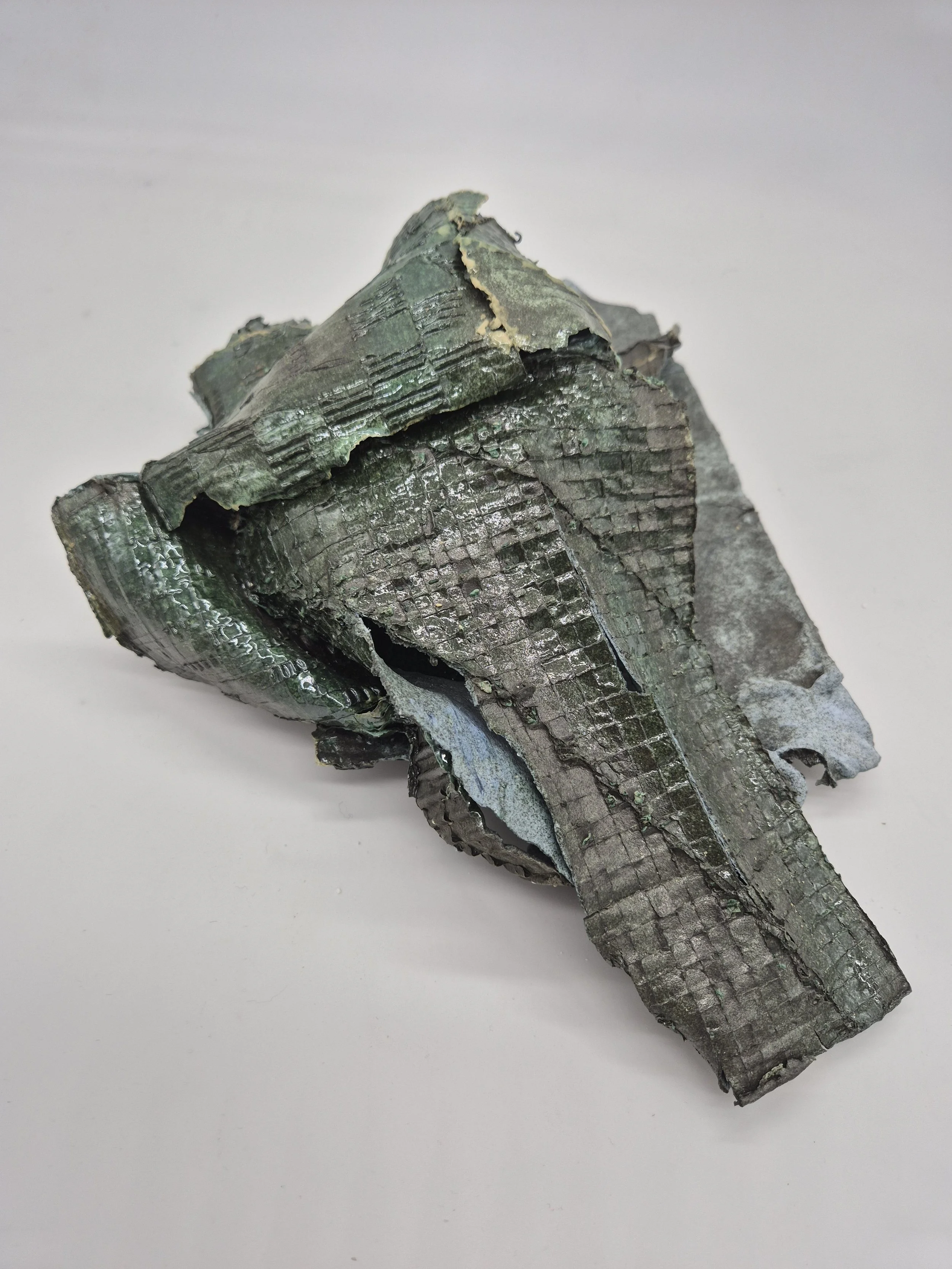 Abstracte keramiek, lijkend op verfrommeld karton met glanzende, groene buitenkant. Het oppervlak vertoont een patroon van vierkanten en scheuren.