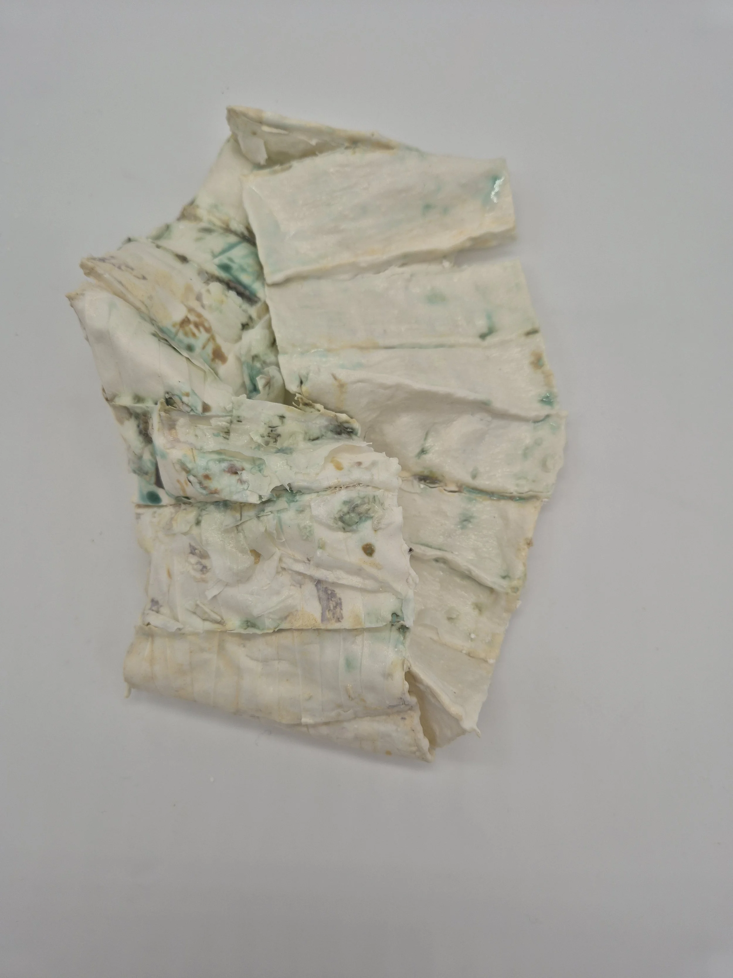 Een verfrommeld stuk wit porselein met groene en beige vlekken op een witte achtergrond.