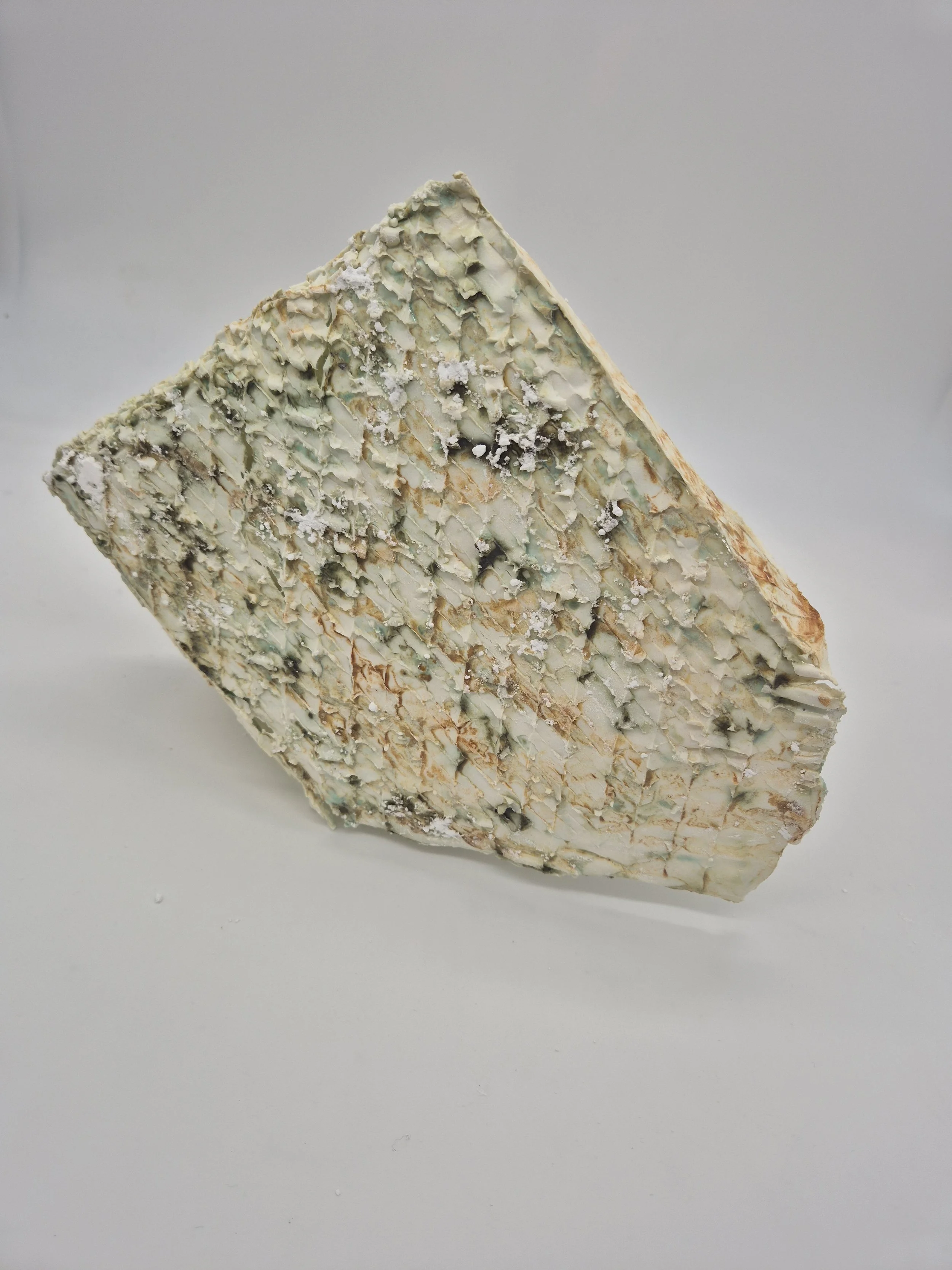 Abstracte keramische sculptuur dat lijkt op een stuk blauwe kaas op een witte achtergrond.