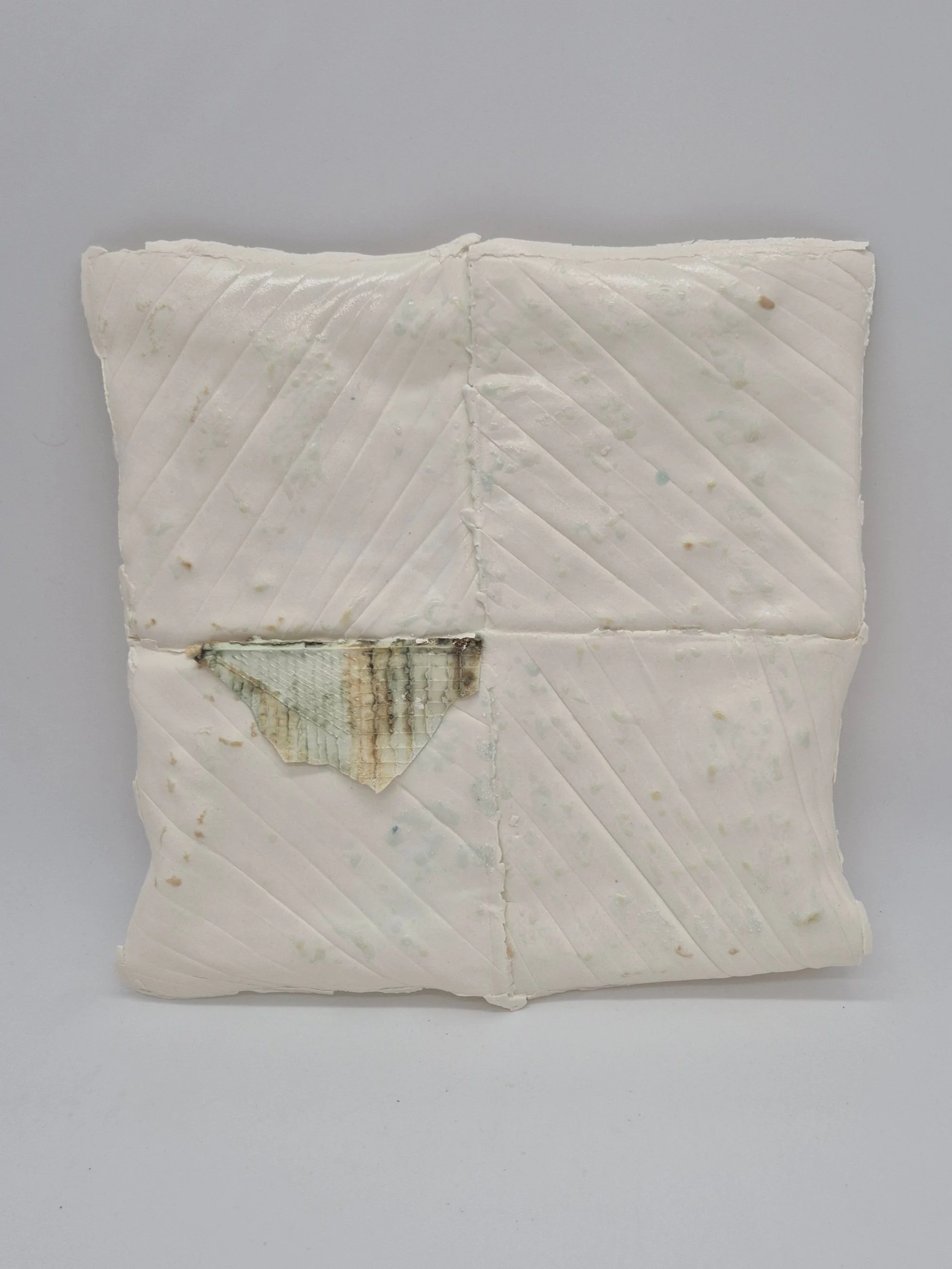 Keramiek object dat lijkt op vierkante opgevouwen witte stof met licht gekleurde vlekken en een doorkijkje naar de geribbelde binnenkant