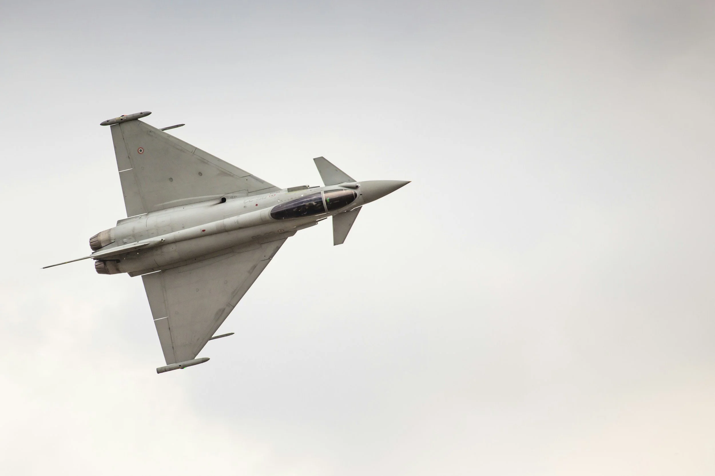 A fighter jet flying in cloudy sky, seen from below at an angle.