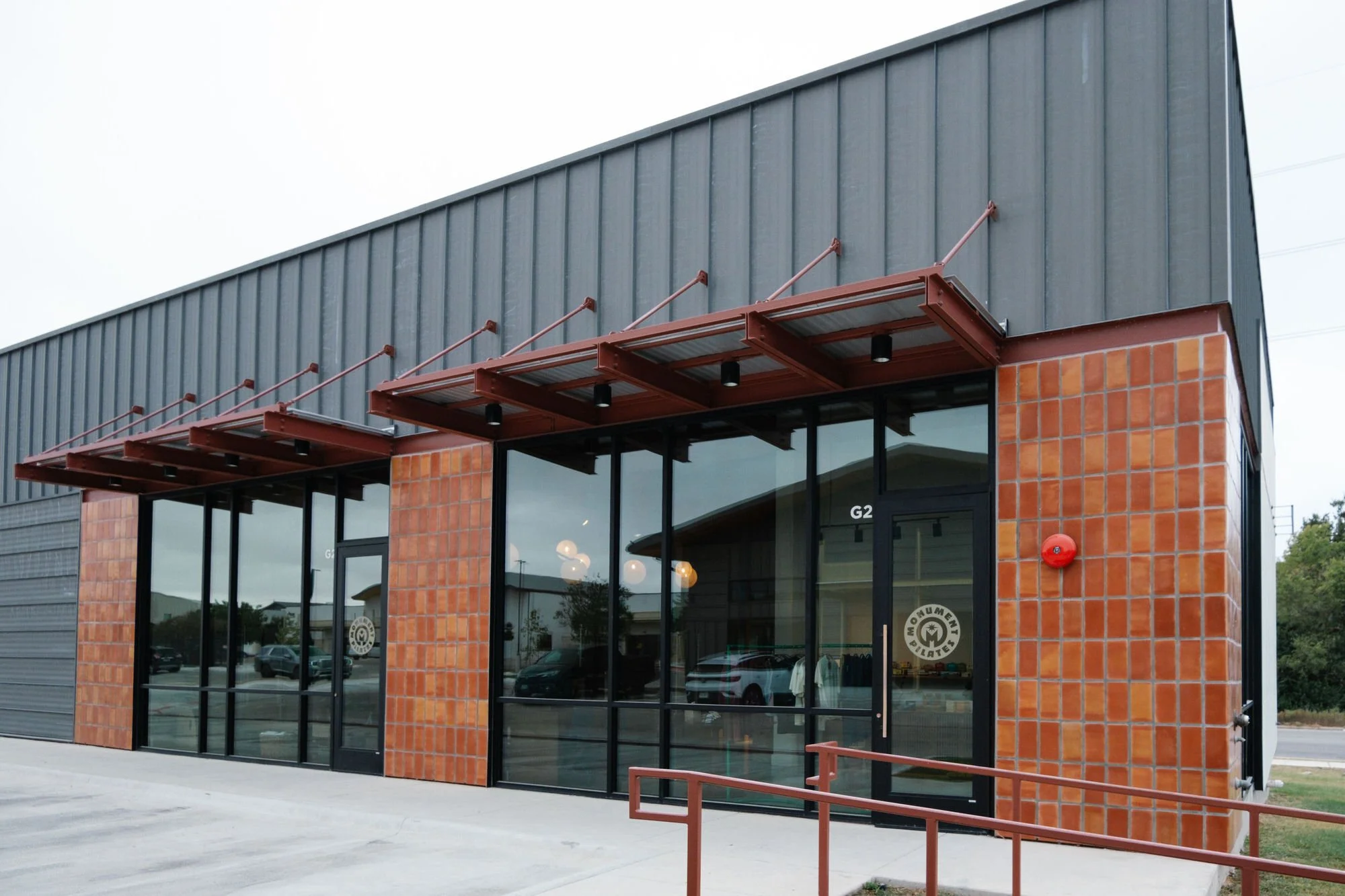 Exterior view of Monument Pilates studio in Pfugerville, TX with large glass windows, brick accents, metal awnings, and a small ramp at the entrance.