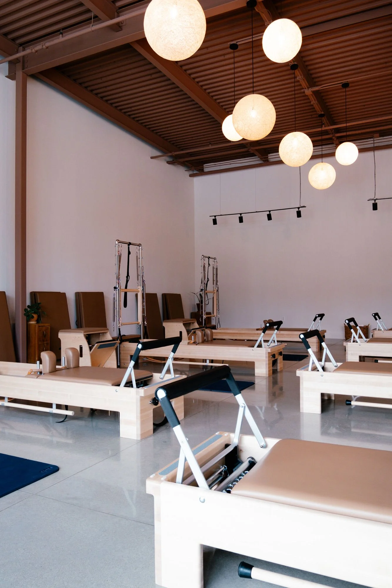 Monument Pilates in Plugerville, TX with reformer Pilates equipment illuminated by spherical hanging lights on a wooden ceiling.