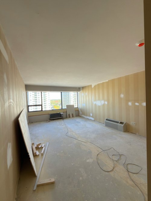 Room under renovation with striped wallpaper partly removed and a plywood sheet leaning against the wall