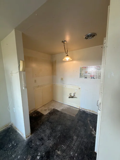 Kitchenette during demolition with bare walls and exposed plumbing fittings