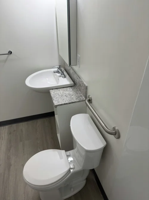 Corner of a small accessible bathroom with wall sink, grab bar and toilet