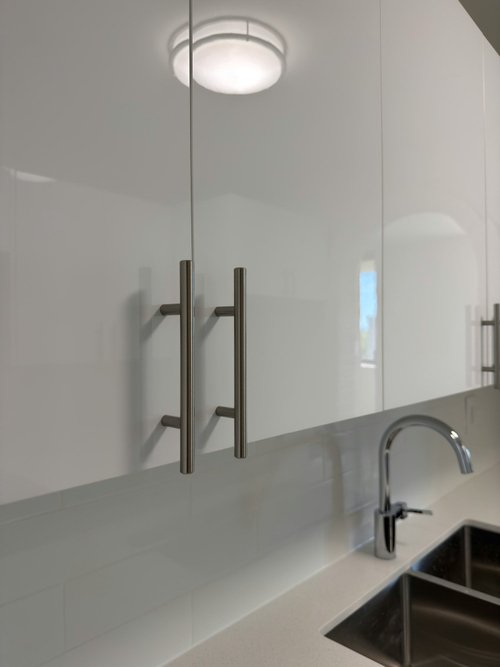 Close-up of white glossy cabinets with bar handles beside a chrome faucet