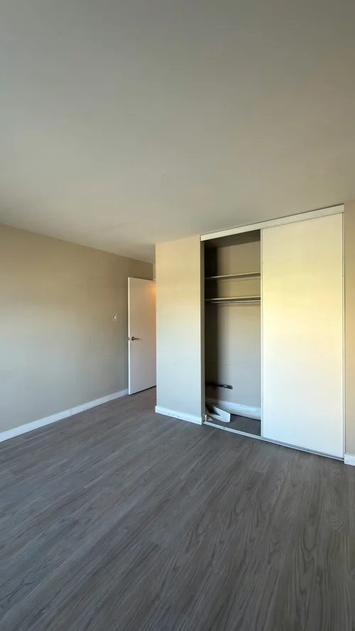 Bedroom with wood-look plank floor, beige walls and a sliding-door closet