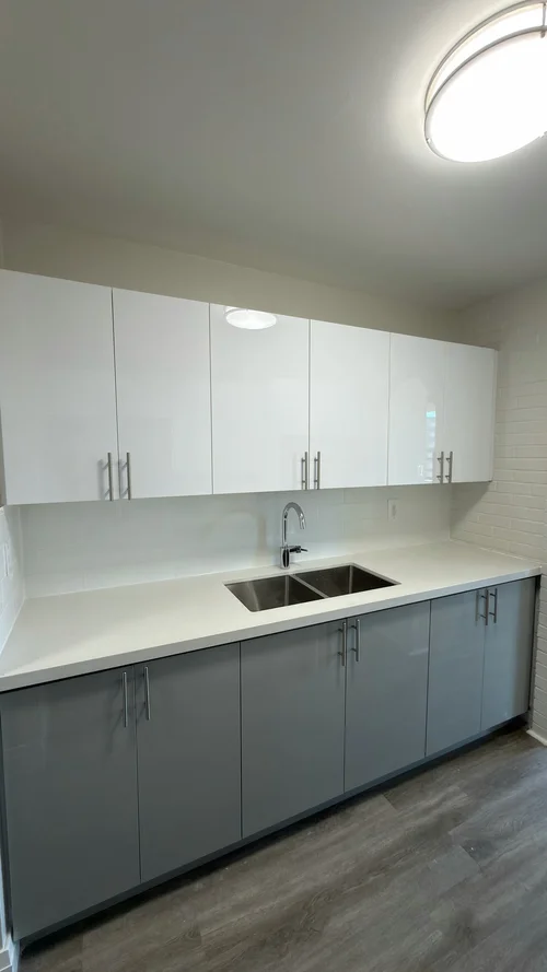 Finished kitchen with white upper cabinets, grey base cabinets and a double sink