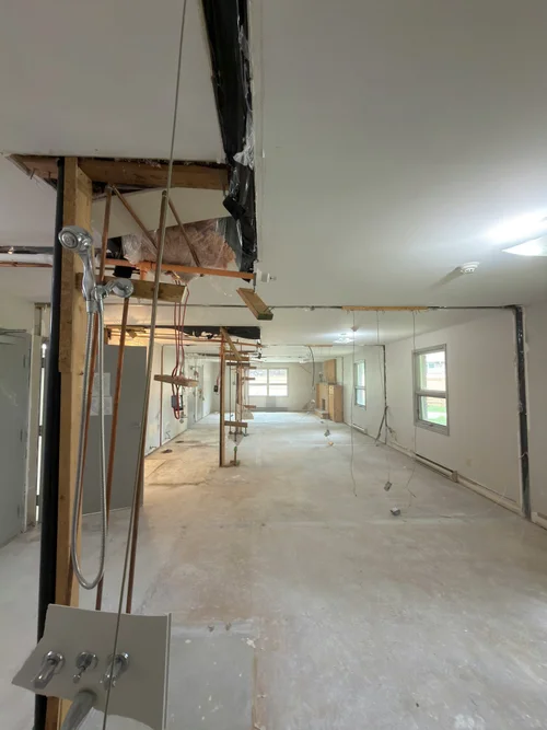 Room during demolition with open ceiling, exposed copper pipes and wood framing