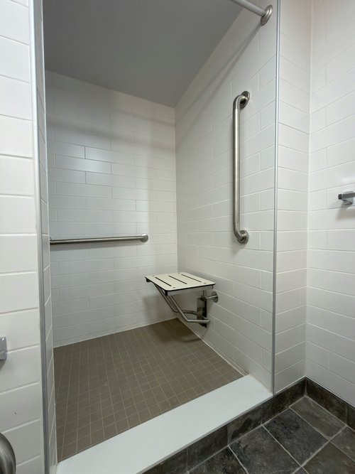 Walk-in shower with white subway tile, fold-down seat, two stainless grab bars and a low curb