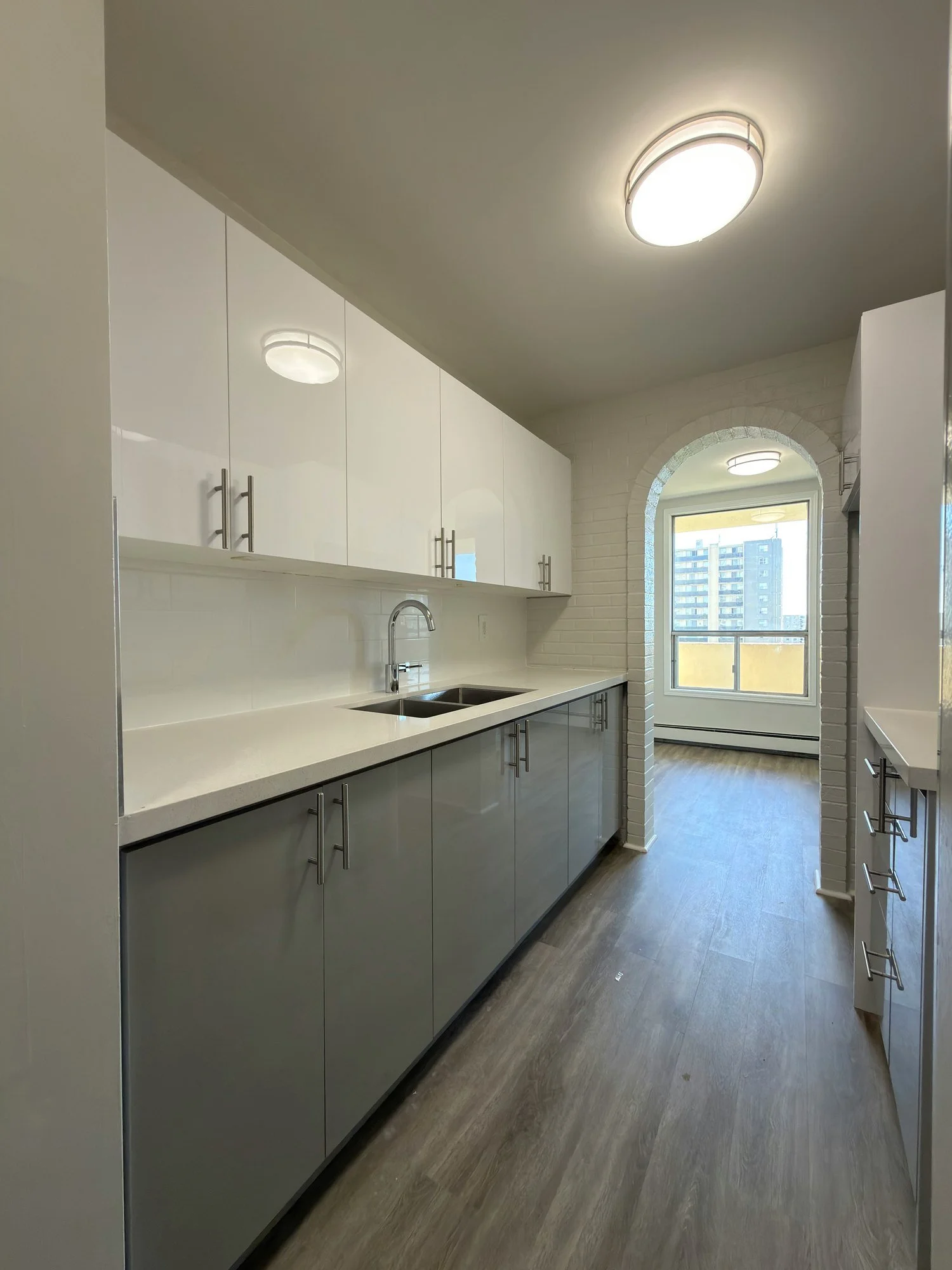 Finished galley kitchen with white gloss upper cabinets, grey base cabinets and a light counter over a double sink