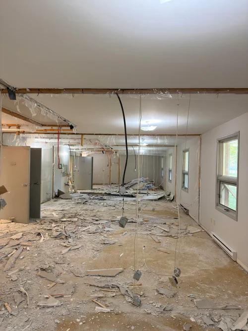 Gutted room with drywall debris on floor and wood framing overhead