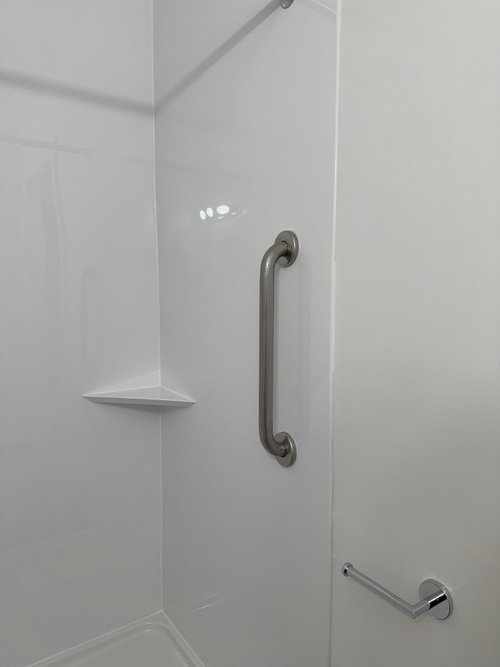 Shower with stainless grab bar and white corner shelf on smooth wall panels