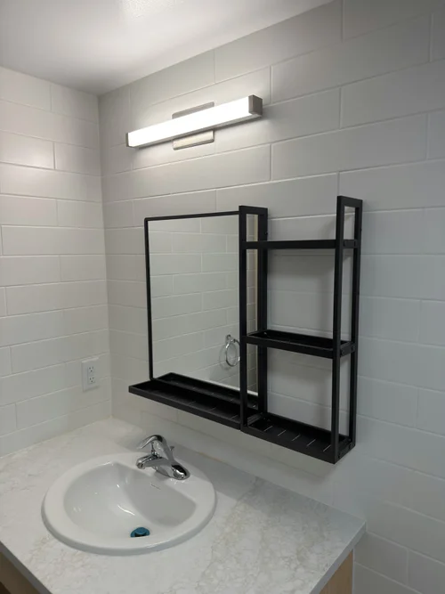 Finished bathroom with black wall shelf, light counter and white tile