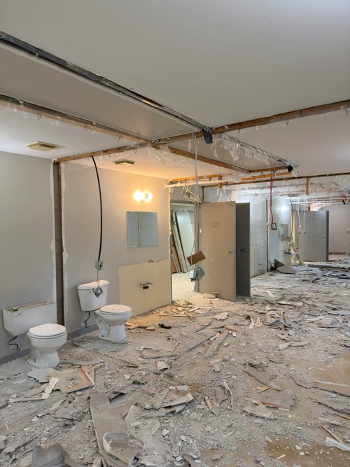 Bathroom during renovation with debris on the floor and two toilets in place
